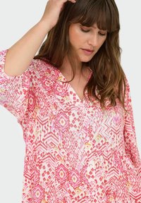 Blusa leggera rosa con motivo geometrico multicolore, scollo a V, maniche lunghe e dettagli con bottoni. Tessuto morbido e vestibilità rilassata.