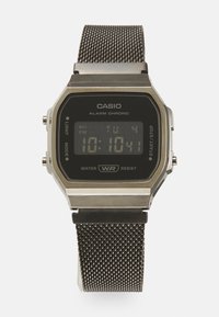 Montre numérique Casio avec un écran rectangulaire noir, boîtier en métal argenté, bracelet en acier inoxydable en maille, dotée d'une alarme et d'une résistance à l'eau.