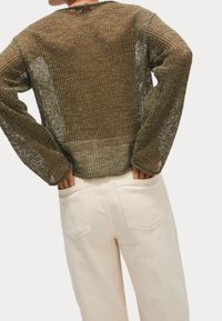 Maglione aperto color verde oliva, con maniche lunghe e scollatura ampia, abbinato a jeans crema chiara con tasche a toppa.