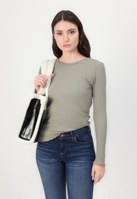 Hosszú ujjú olajzöld bordázott felső, sötétkék farmerral párosítva. A táska téglalap alakú, fehér bolyhos pánttal és fényes fekete felülettel.