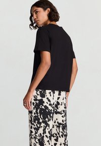 T-shirt nera a maniche corte con vestibilità rilassata; indossata con pantaloni chiari caratterizzati da un motivo astratto bianco e nero.