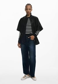 Veste bomber en simili cuir noir sur un haut à rayures noir et blanc à manches longues, associée à un jean large bleu foncé et des chaussures claires.