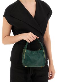 Borsa a tracolla verde in pelle con forma arrotondata, borchie decorative dorate sui lati e due manici corti. Indossata con un abbigliamento nero.
