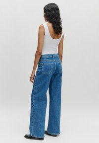 Wijdvallende blauwe denim jeans met een hoge taille en twee achterzakken, gecombineerd met een aansluitend wit tanktop. Soepele textuur en casual ontwerp.