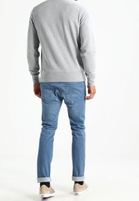 Sudadera gris con cuello redondo, puños acanalados, combinada con jeans ajustados de color azul claro y zapatillas color beige; costuras visibles y detalles de diseño casual.