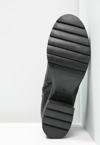 Semelle de chaussure en cuir noir avec un motif rainuré, bout arrondi et talon plat. Présente une texture lisse et un petit logo.