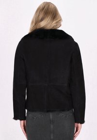 Veste en suède noir avec col en fausse fourrure, design court et détails en couture le long du dos et des manches.
