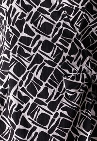 Tissu à motifs noir et blanc présentant des formes et textures irrégulières, avec un aspect froissé et des détails de bord repliés.