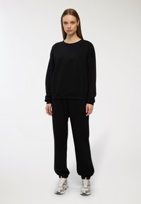 Felpa nera e pantaloni abbinati in tessuto morbido. Vestibilità ampia con polsini a coste, caratterizzati da un design semplice e senza motivi visibili.