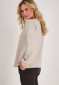 Lichtbeige lange mouwen top met een ontspannen pasvorm, voorzien van een ronde halslijn en elastische manchetten. Gecombineerd met donkere, strakke broeken.