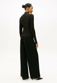 Strakke zwarte turtleneck met lange mouwen, gecombineerd met wijde zwarte jeans, met een gladde textuur en minimalistisch ontwerp.