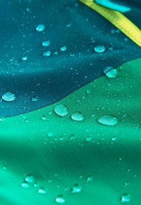 Material impermeabil în nuanțe de teal închis și verde, cu picături de apă pe suprafață, evidențiind textura sa hidrofugă.