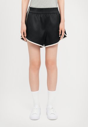 Schwarze Sportshorts mit abgerundetem Saum, weißen Seitenstreifen und einem elastischen Bund. Kombiniert mit weißen Socken und Turnschuhen.