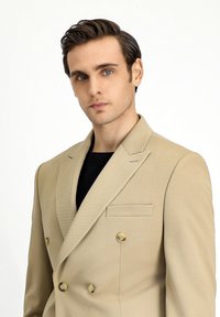 Blazer beige doppiopetto con finitura testurizzata, rever a notched e bottoni in tono oro. Tasche sul petto singole e vestibilità sartoriale.