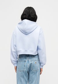 Κοντή φούτερ ζακέτα σε ανοιχτό μπλε βαμβάκι, με κουκούλα, μακριά μανίκια και ριμπ τελείωμα. Συνδυάζεται με τζιν παντελόνι σε μπλε ρίγες με ψηλή μέση.