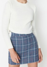 Bílý žebrovaný top s dlouhým rukávem, spojený s modrou kostkovanou sukní s růžovými akcenty. Top má přiléhavý střih se zavazováním po stranách.