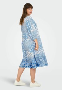 Modra in bela obleka z vzorcem, s tremi četrtinami rokavi, ohlapnim krojem in razširjenim robom, izdelana iz lahkega materiala.