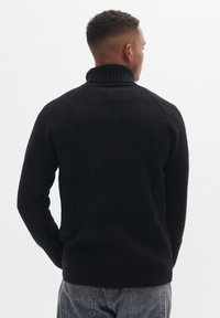 Suéter negro de punto acanalado con cuello alto, mangas largas y dobladillo ajustado. Tejido texturizado con un diseño ceñido al cuerpo.