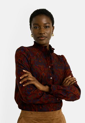 Blusa de manga larga en un rico color burdeos con un patrón paisley en verde y azul. Cuenta con un cuello fruncido y un cierre de botones en la parte delantera. Textura suave.