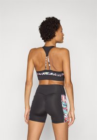 Melnā sporta krūšturis ar racerback dizainu un daudzkrāsainu ziedu rakstu ap siksniņu, apvienots ar melnām augstām šortiem, kuriem ir sānu akcenti.