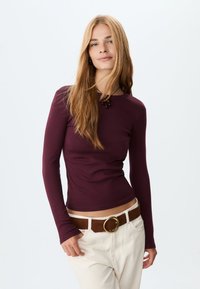 Bordeaux langærmet top med et tætsiddende design, lavet af blødt stof, parret med højtaljede lyse beige bukser og et brunt bælte med en rund spænde.