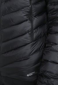 Černá zateplená bunda s prošívaným designem, hladkou texturou, zipovým zapínáním a detailem loga v dolním rohu.