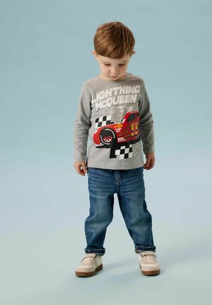Chemise grise à manches longues avec un graphisme de voiture de course rouge et le texte « Lightning McQueen », associée à un jean en denim bleu et des chaussures de couleur claire.