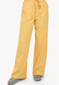 Geel gestreepte wijde broek met een trekkoord in de taille; heeft dunne roze lijnen en een gladde, lichte stof. Gepaard met blauwe hakken.