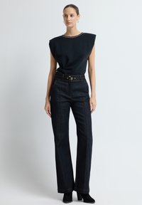 Tmavě modré riflové kalhoty s rozšířením a oranžovým prošíváním, spárované s černým topem s krátkým rukávem se šněrováním s kovovými akcenty.