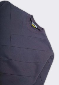 Felpa crewneck trapuntata grigio scuro con cuciture visibili e colletto a coste, posata su una superficie chiara.