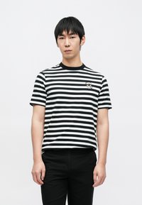 Czarna i biała koszulka w paski z okrągłym dekoltem, krótkimi rękawami i małym nadrukiem na lewej piersi. Połączona z czarnymi spodniami.