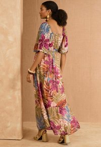 Maxi-jurk in een bloemenpatroon met levendige kleuren, waaronder roze, groen, geel en blauw; heeft vloeiende mouwen en een tailleriem.