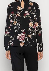 Svart blommig blus med långa ärmar, nyckelhålsdetalj på ryggen och en blandning av färgglada blommönster på mjukt tyg.