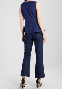 Marinblå ärmlös topp med peplumdesign, tillsammans med mörk denim-flared jeans. Outfiten kompletteras av svarta snygga högklackade sandaler.