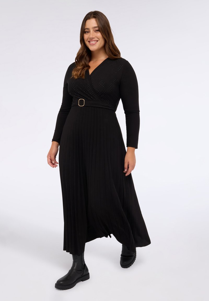 Rochie neagră cu mâneci lungi, cu design înfășurat, featuring un tiv texturat, fustă pliată și un accent din curea circulare. Asortată cu cizme negre până la glezne.