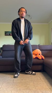 Giacca nera con zip sopra una maglietta bianca, abbinata a jeans grigi scuri e scarpe da ginnastica bianco e nere. Un morbido polpo arancione è vicino.