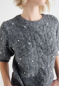 Γκρι πλεκτό πουλόβερ με κοντά μανίκια, που διαθέτει μια μαλακή, υφασμένη επιφάνεια και κοσμήματα από μαργαρίτες διάσπαρτα σε όλη την σχεδίαση.