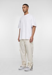 T-shirt oversize bianco in cotone, pantaloni beige morbidi e scarpe da ginnastica grigie. Design semplice con maniche corte e silhouette rilassata.