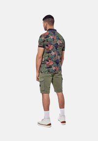 Polo shirt met een levendig bloemenpatroon in groen en roze, gecombineerd met olijfgroene cargoshorts. Witte sneakers en enkelsokken maken de outfit compleet.