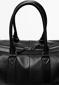 Zwarte leren weekendtas met twee afgeronde handvatten en een zilveren rits die gedeeltelijk gesloten is aan de bovenkant in het midden.