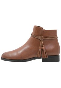 Bottines en cuir marron avec une texture lisse, détail tressé en haut et des pompons, dotées d'un petit talon carré et d'un bout arrondi.