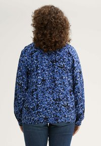 Langärmlige Bluse mit einem blau-schwarzen abstrakten Muster, aus glattem Stoff mit lockerer Passform und gerafftem Detail auf der Rückseite.