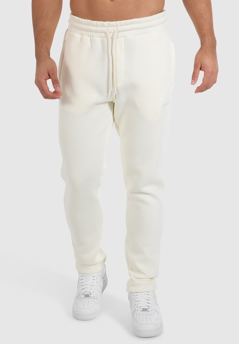 Hellbeige Jogginghosen mit einem Kordelzugbund, seitlichen Taschen und einem schmal zulaufenden Bein-Design. Kombiniert mit weißen Sneakern.