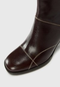 Stivaletto in pelle marrone alla caviglia con punta arrotondata, caratterizzato da cuciture a contrasto e texture liscia. Design elegante e tacco basso.