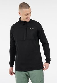 Čierny pulóver s dlhým rukávom a zipsom pri golieri, s textúrovanou prsnou časťou a jemným logom, spárovaný so svetlozelenými nohavicami.