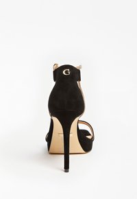 Sandale à talons hauts en daim noir avec un accent logo doré. Présente un talon fin, une conception à bout ouvert et de fines lanières. Texture lisse.