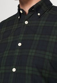Grön och svart rutig skjorta med knapp-ner krage och kontrasterande beige knappar, tillverkad av texturerad tyg.