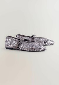 Glitzernde silberne Ballerinas mit einem Obermaterial aus Pailletten, flacher Sohle und einem passenden Riemen über dem Fuß. Spitz zulaufendes Design.