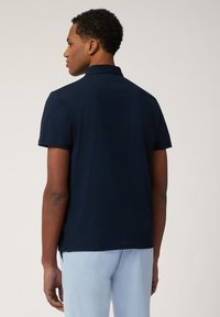 Marineblaues Poloshirt mit kurzen Ärmeln und klassischem Kragen, das eine glatte Textur und dezente Nahtdetails am Rücken bietet.