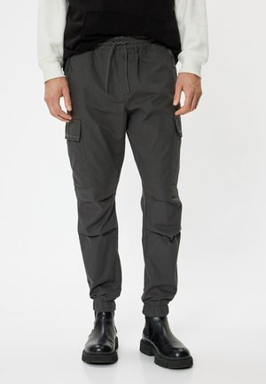 Graue Cargo-Hosen mit elastischem Bund, verstellbarem Zugband, Seitentaschen und gesäumten Knöcheln, kombiniert mit schwarzen Stiefeln.